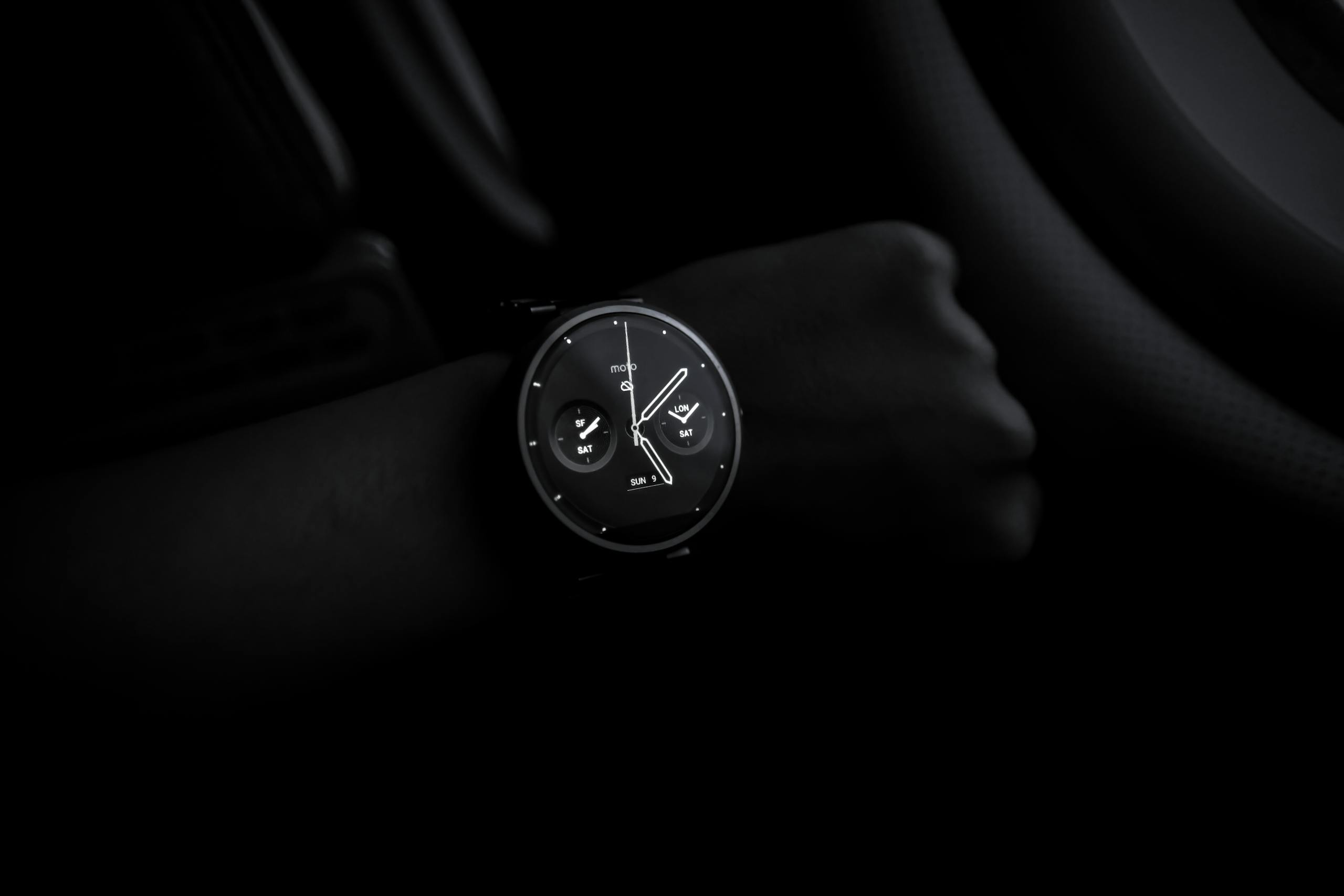 Simbramento A sleek Moto 360 smartwatch showing time on a wrist in a dimly lit setting, emphasizing its modern design and technology.