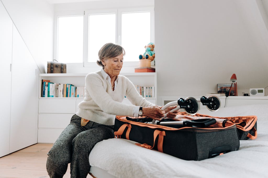 Impupdates.comwow Independence Elderly woman packing a rollator into a suitcase at home, preparing for a trip.