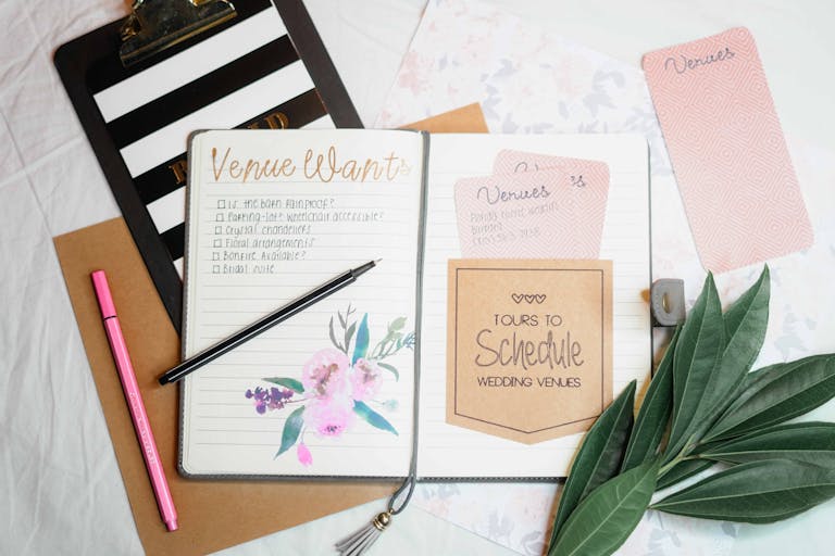 Bastinews.xyz Flat lay of wedding planning materials including a journal, leaves, and stationery.