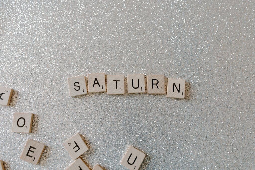 Kinervus Scrabble tiles forming the word SATURN on a sparkling glitter background, space theme.
