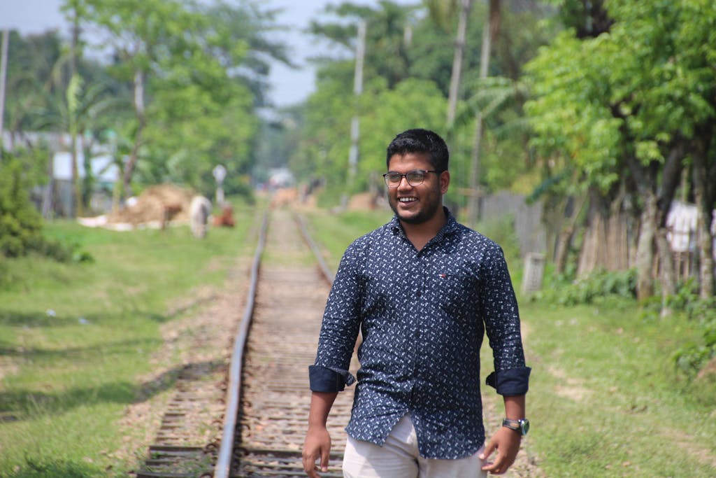 SEO by HighSoftware99.com: Smiling man casually walking on railway tracks surrounded by lush greenery in Jamalpur, Bangladesh.