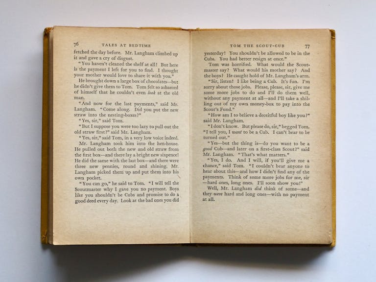 BinusCX Kinervus Vintage book opened to pages 76-77, displaying classic literature text in soft lighting.