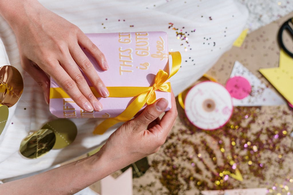 RN Fundamentals 2016 A festive gift wrapped with a yellow ribbon and the message 'This gift is gluten-free' amidst sparkles and decorations.