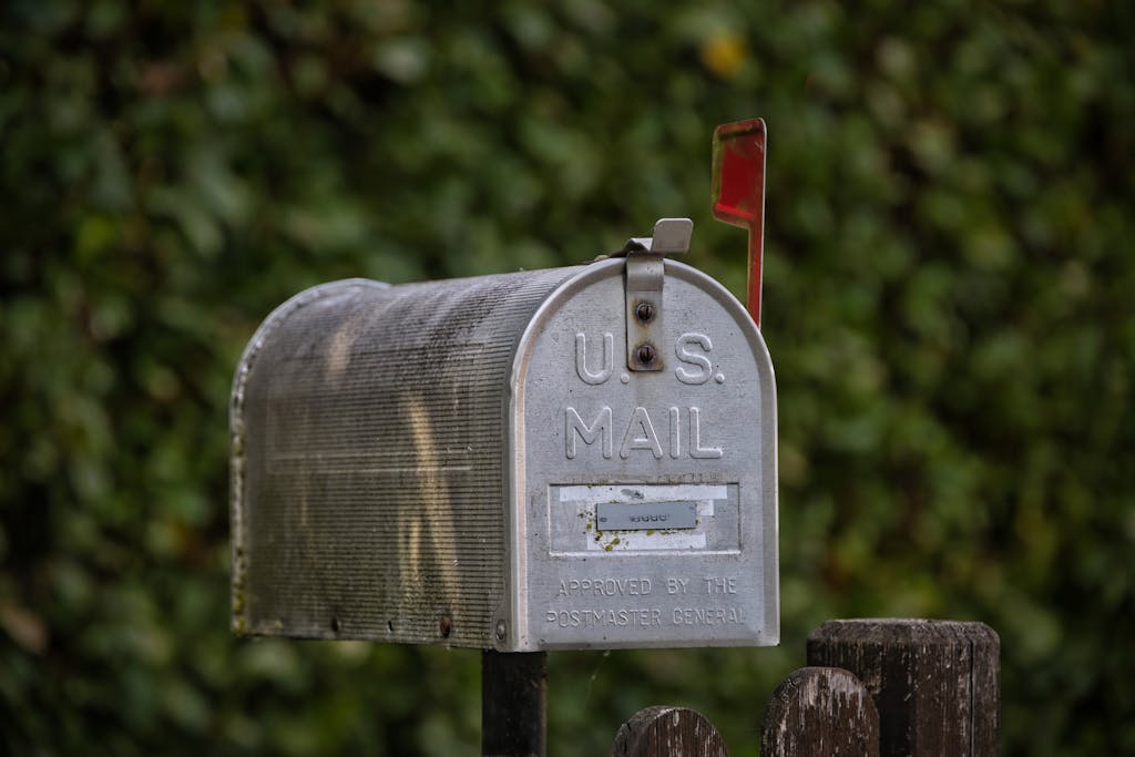  The Globe and Mail  A traditional U.S. mailbox with red flag against a lush green blurred background.