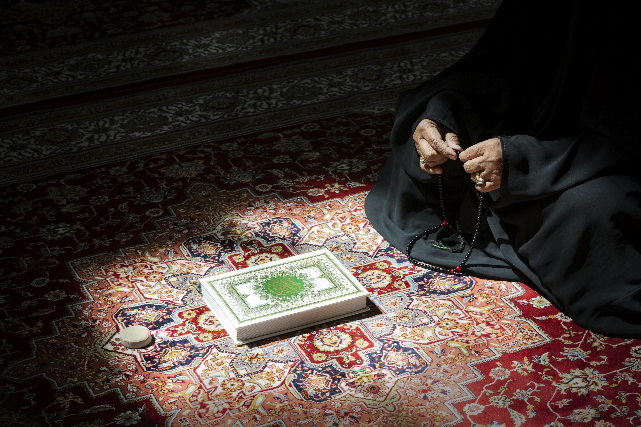 TRIOS 5 Invisalign Submission A woman in serene prayer holding beads beside an ornate Quran on a colorful rug.