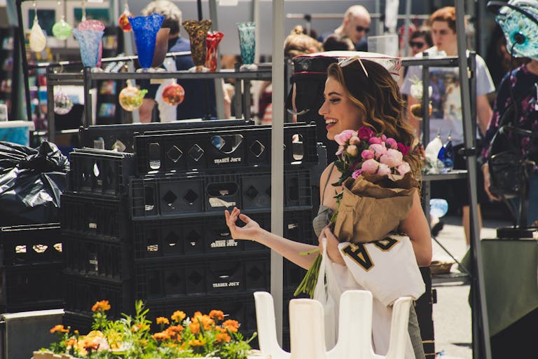 Shop Spring Vase A woman joyfully shops at an outdoor market, holding roses.