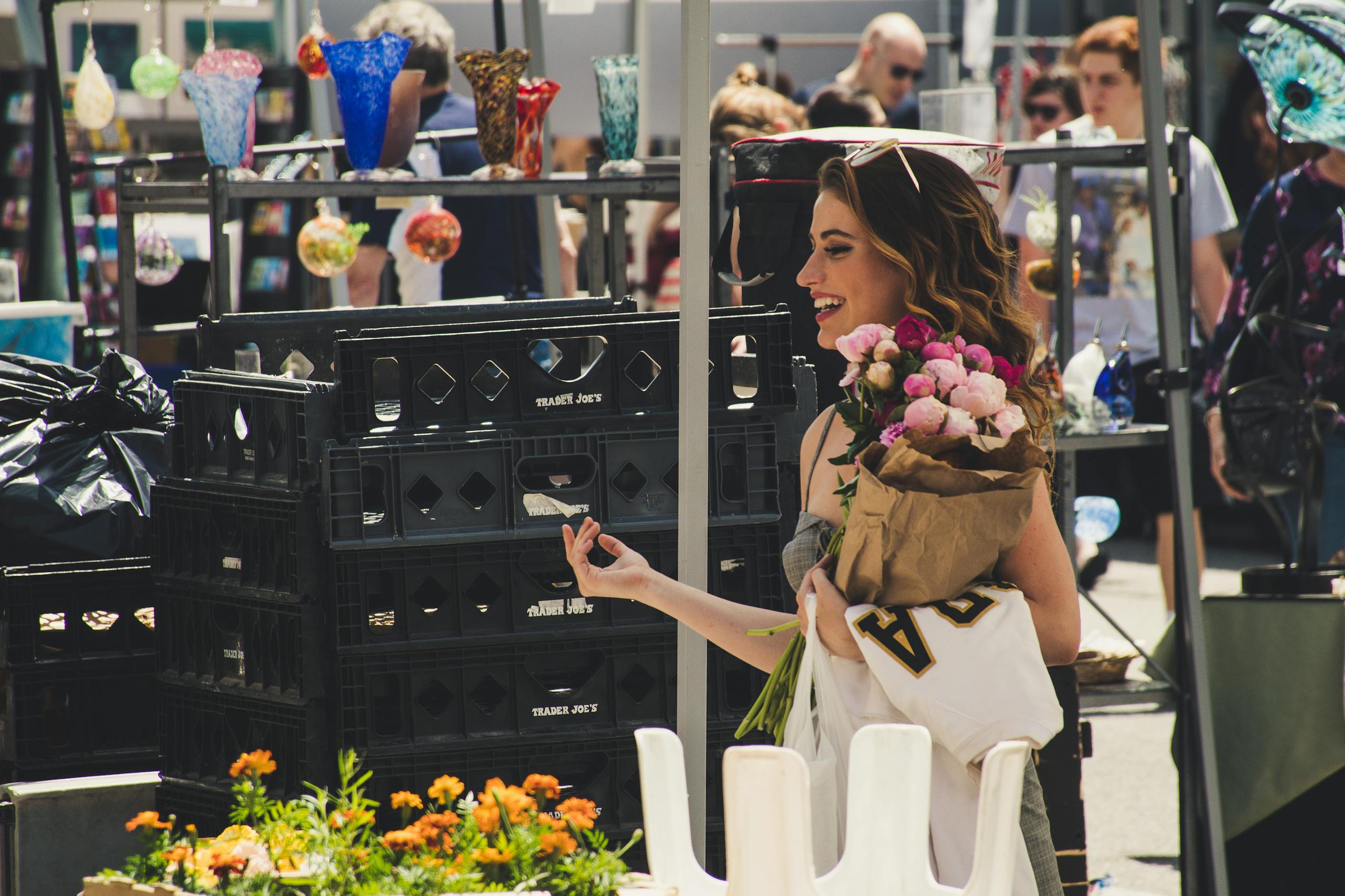 Shop Spring Vase A woman joyfully shops at an outdoor market, holding roses.