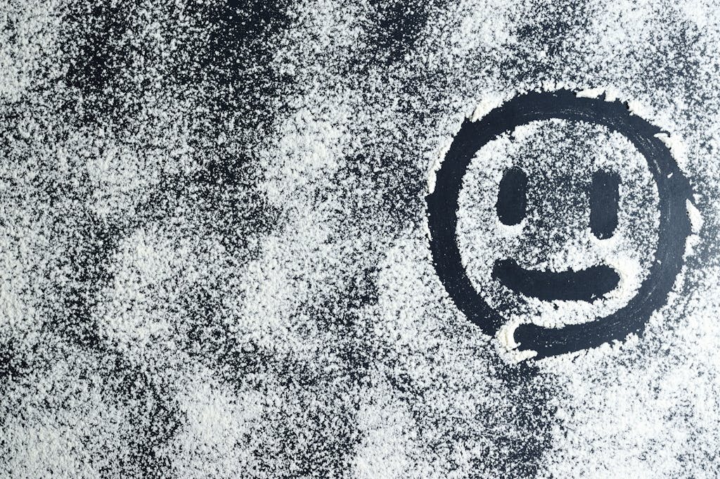 Emfyteymata Artistic smiley face drawn through white powder on a black surface, creating an abstract texture.