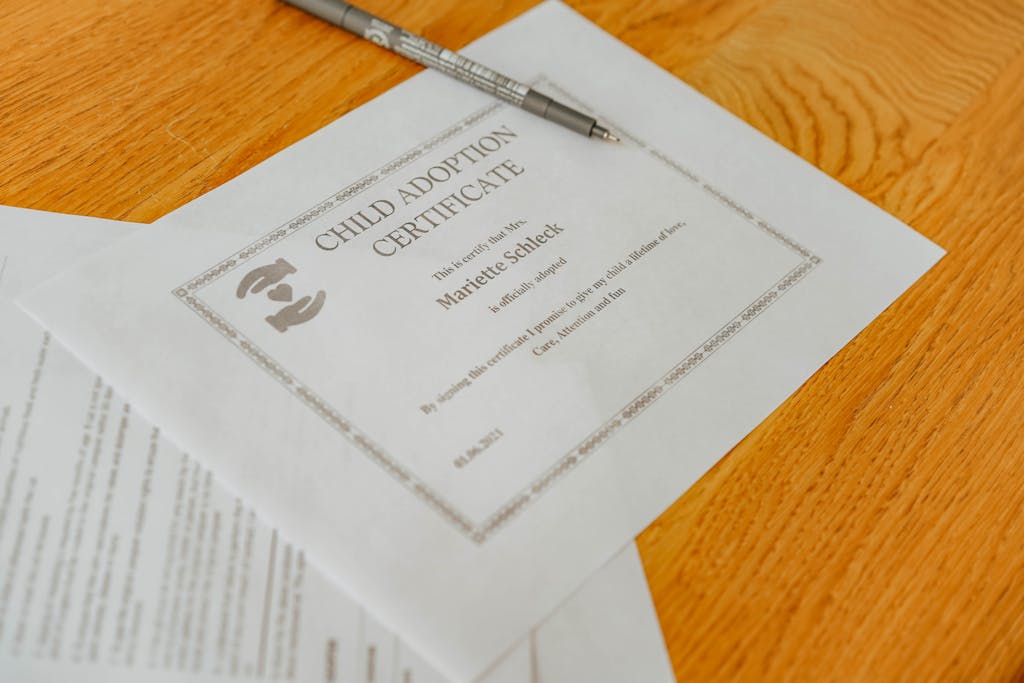 Six Sigma Certification Online Close-up of a child adoption certificate and documents with a pen on a wooden table.
