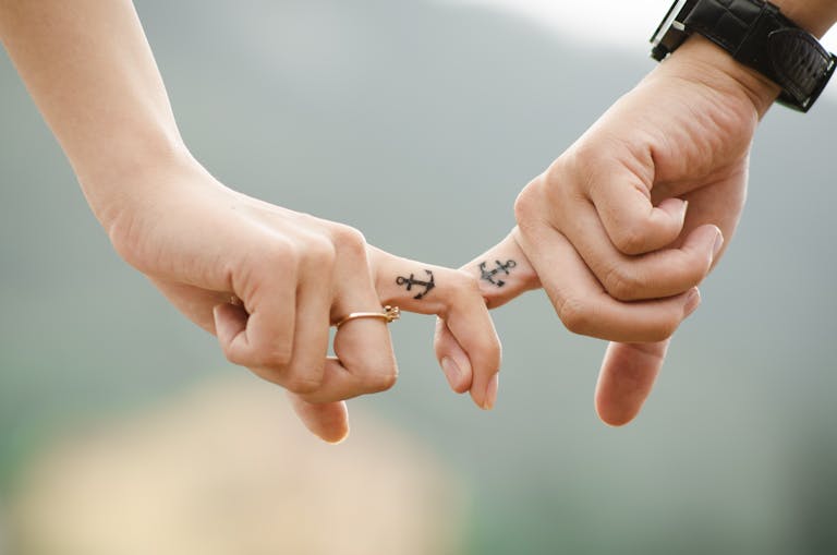 JuntosSeguros Close-up of a couple holding hands, featuring anchor tattoos symbolizing love and connection.