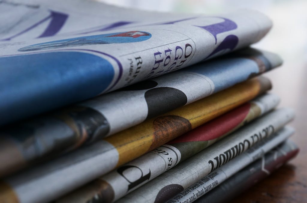 ventsmagazine Close-up of a stack of colorful newspapers on a wooden table, showcasing print media.