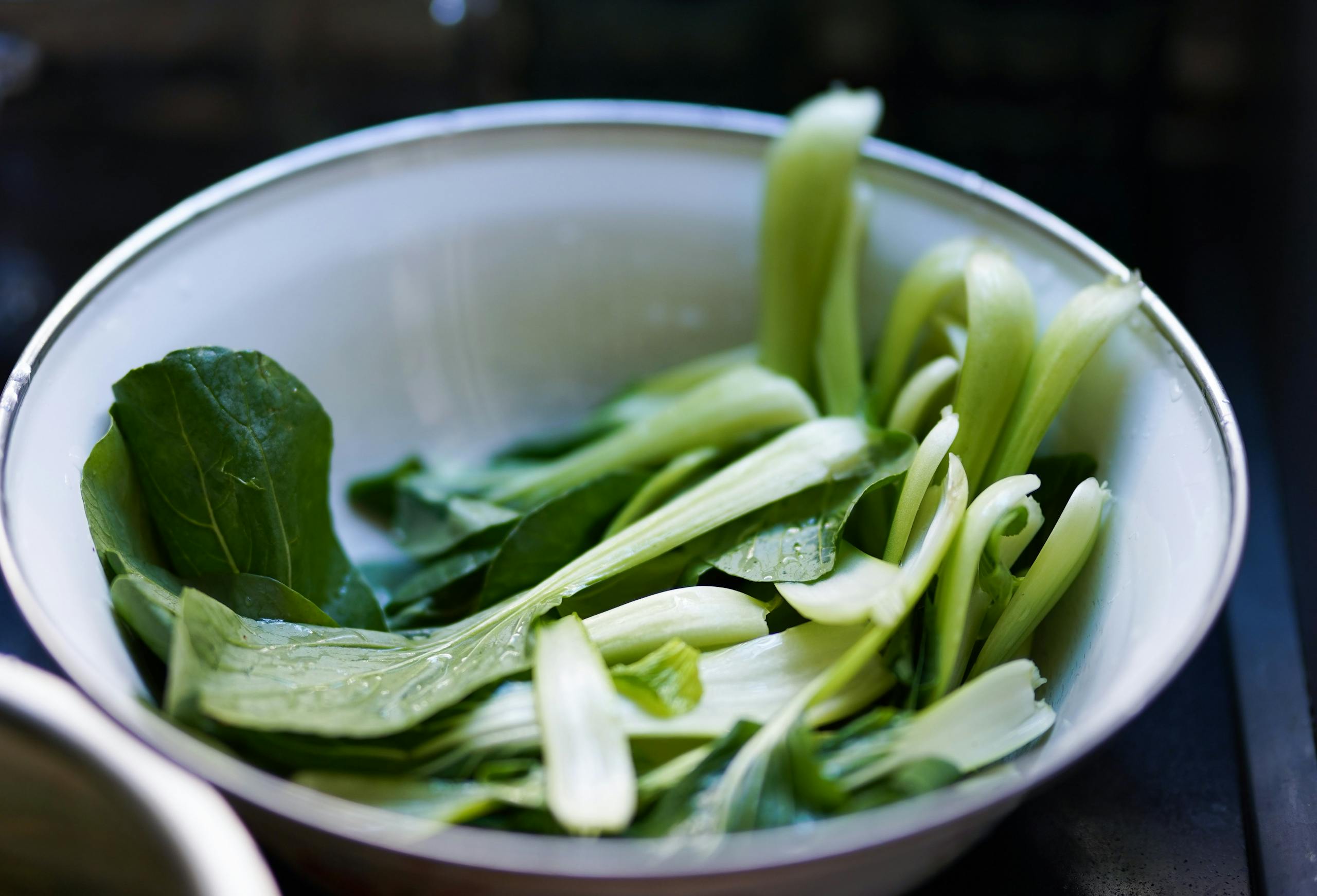 Pak vs Ind Close-up of fresh pak choi leaves in a white bowl, ready for a healthy meal.