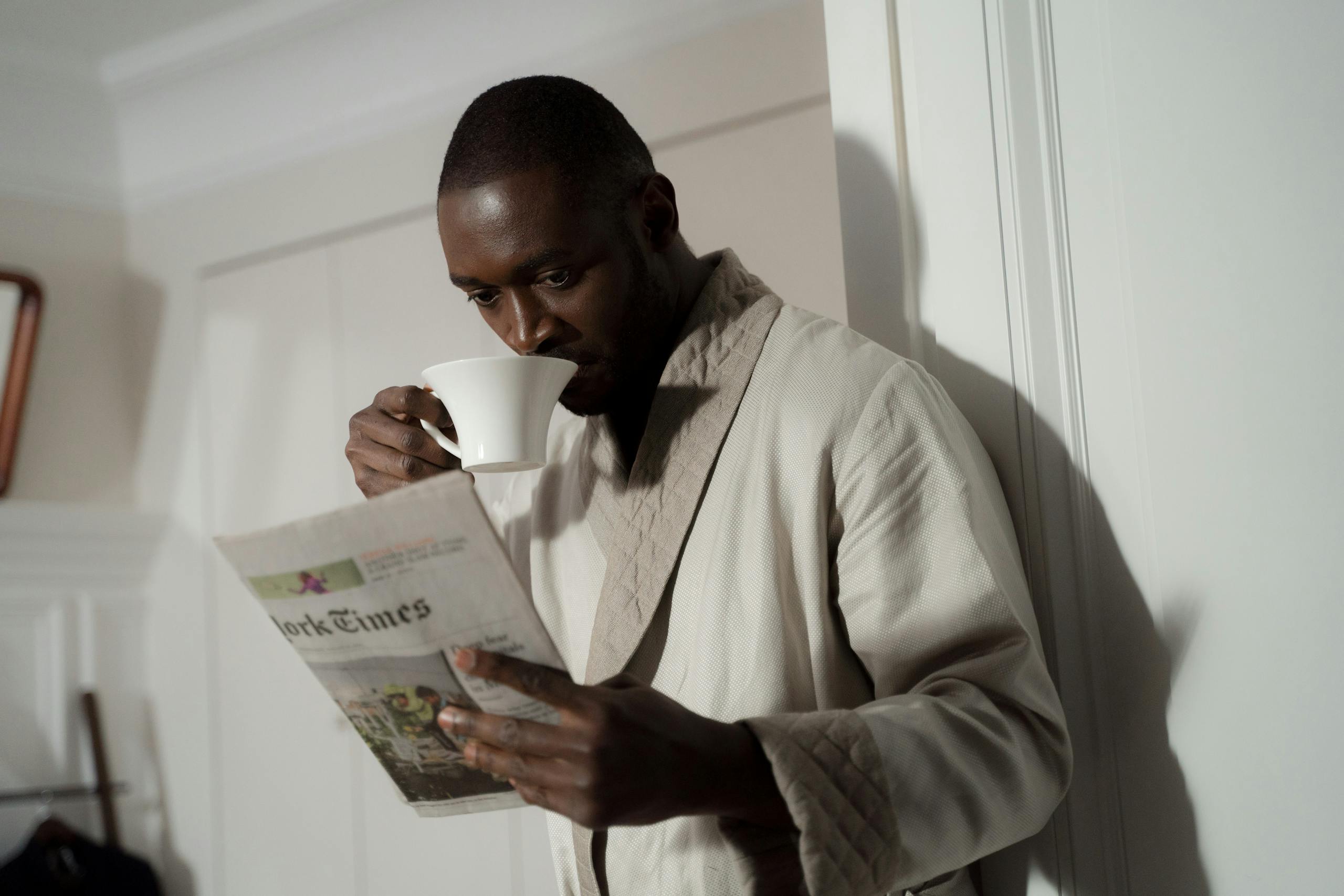 Newstook Man in a bathrobe enjoys coffee and reads a newspaper indoors.