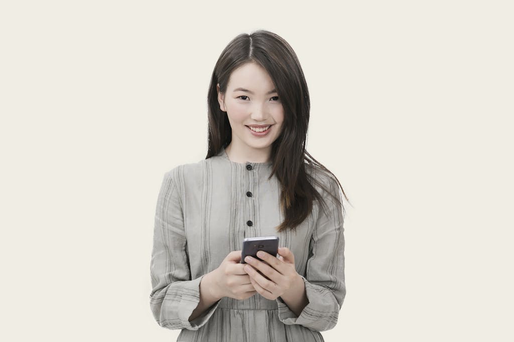 SocialMediaGirl Smiling woman with long hair using her smartphone, wearing a casual outfit against a simple background.