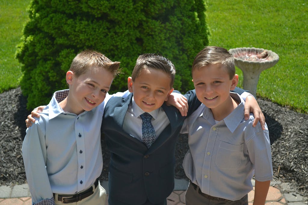 JuntosSeguros Three boys in formal shirts smiling together outdoors in a sunny garden.