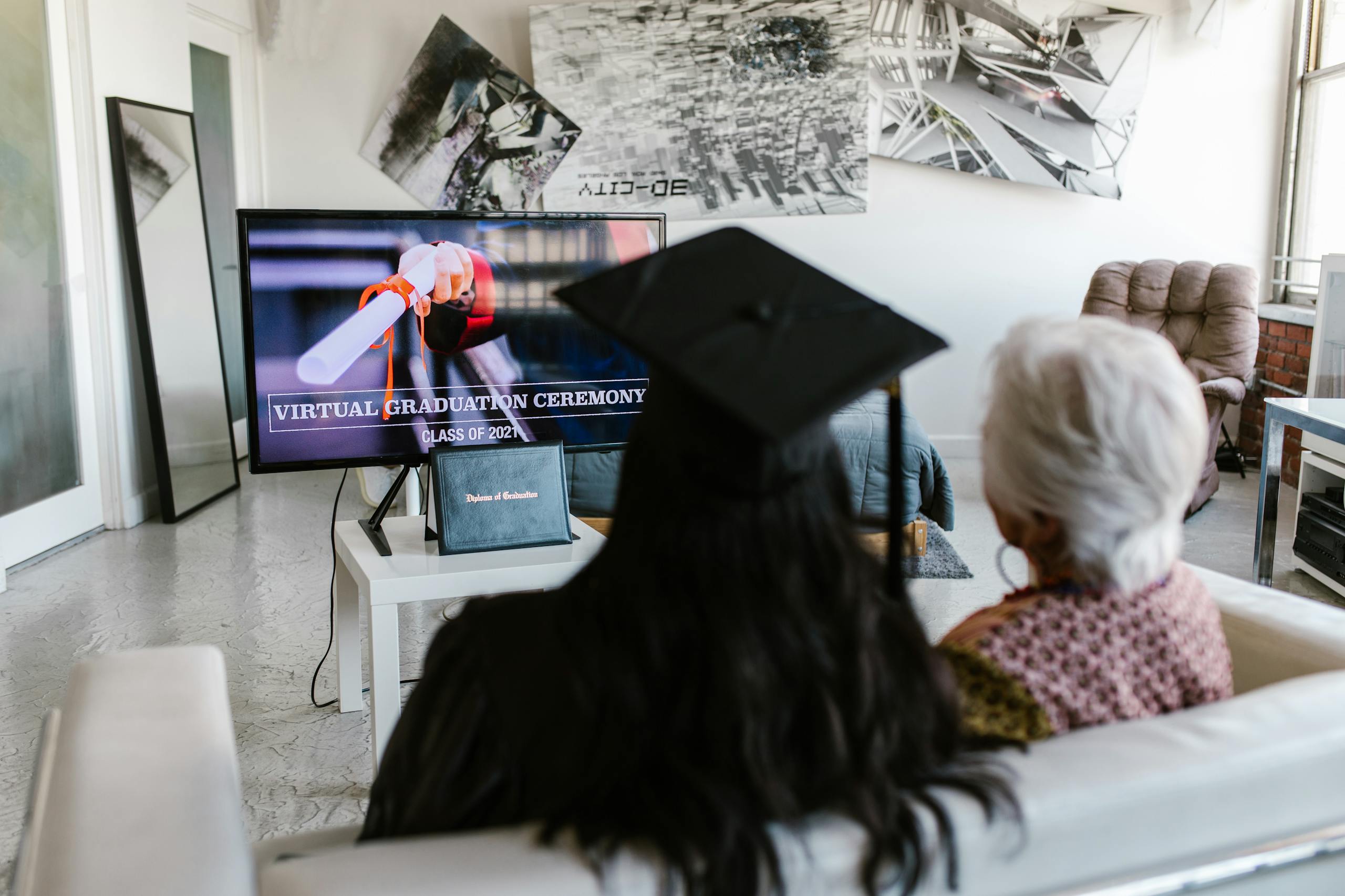 Six Sigma Certification Online Two people watching a virtual graduation ceremony together at home, capturing the new normal of online celebrations.