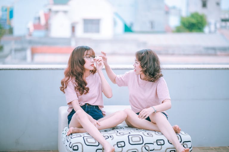 SocialMediaGirl Two sisters in casual outfits laughing and interacting during a sunny day on a rooftop.