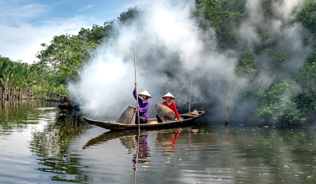 Dampfreis Two women in conical hats fishing on a river with a wooden boat in rural Vietnam.